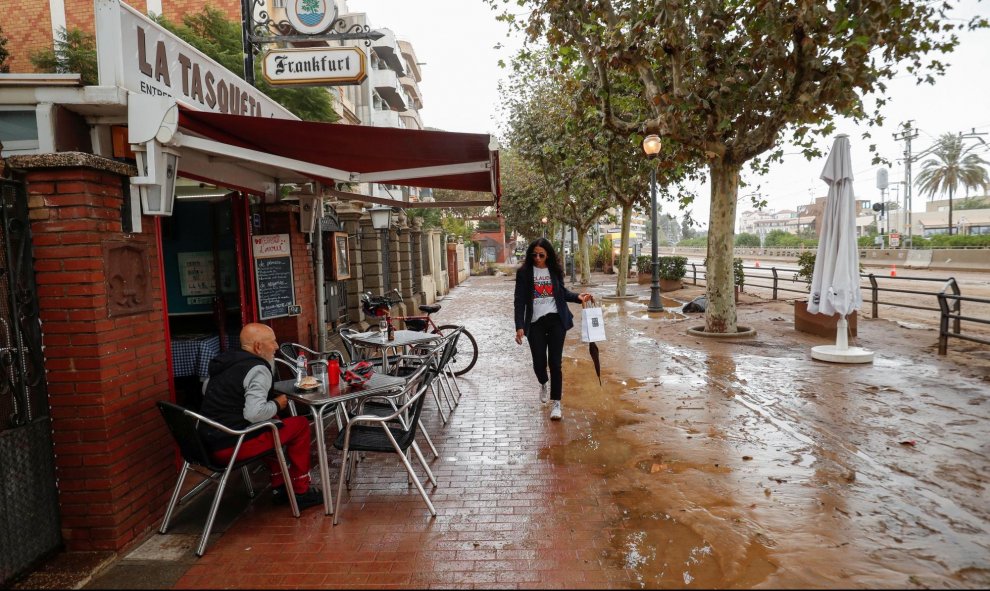 23/10/2019.- Una mujer camina junto a un bar por una calle cubierta de lodo después de las inundaciones causadas por lluvias torrenciales en Arenys de Mar. REUTERS / Albert Gea