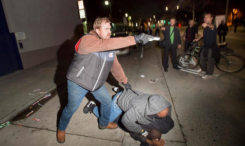 Un oficial de policía de paisano apunta contra su arma contra los manifestantes en Oakland (California) tras ser atacados por algunos de los congregados. Protestan por la decisión de la justicia de exonerar a Darren Wilson, un policía blanco de Ferguson,