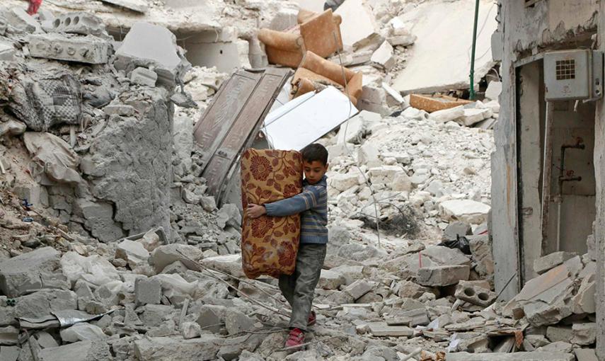 Un niño lleva sus pertenencias mientras camina sobre los escombros en el barrio de al-Kalaseh, de Alepo. // HOSAM KATAN (REUTERS)