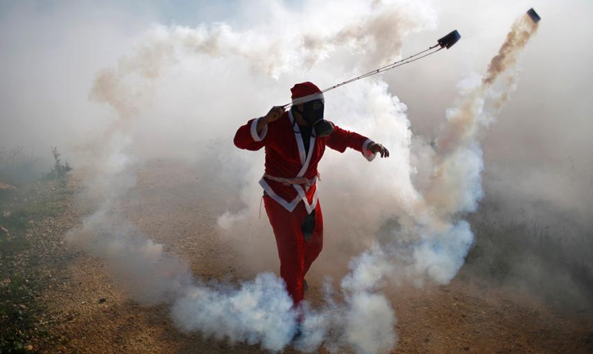 Un manifestante palestino, vestido como Santa Claus, utiliza una honda para devolver un bote de gas lacrimógeno disparado por las tropas israelíes durante los enfrentamientos tras una protesta contra los asentamientos judíos en la aldea cisjordana de Bili