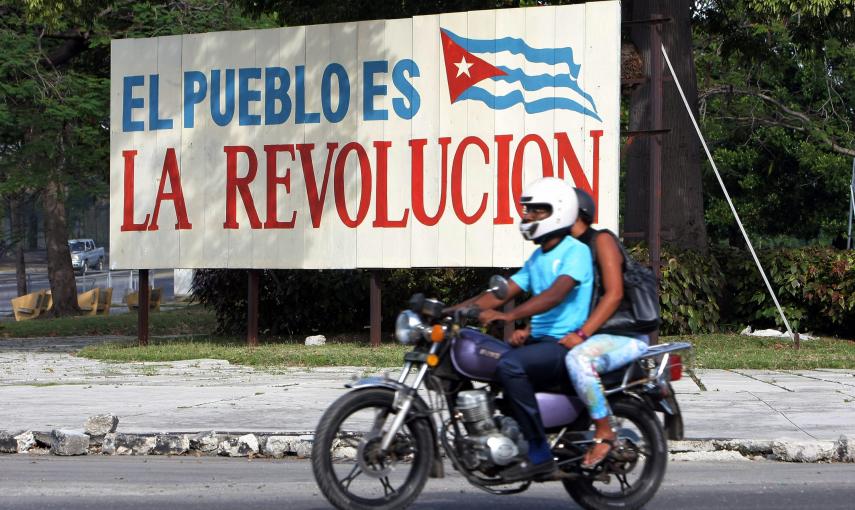 Dos personas pasan en una moto delante de un cartel alusivo a la revolución cubana, en La Habana. EFE/Ernesto Mastrascusa