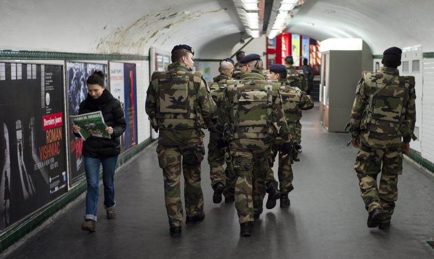 Una mujer lee laúlrima edición del semanario satírico 'Charlie Hebdo' mientras se cruza con un grupo de soldados franceses que patrulla en el interior de la estación de metro de Trocadero en París. EFE/Yoan Valat