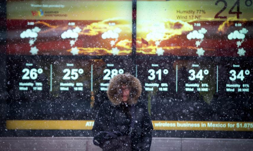 Una mujer delante de una pantalla gigante mientras cae la nieve. REUTERS/Mike Segar