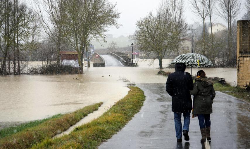 Varias personas caminan por la carretera de acceso al pueblo de Villodas que se encuentra inundada debido al desbordamiento del río Zadorra, tras las lluvias registradas en la región. -EFE/ADRIAN RUIZ DE HIERRO