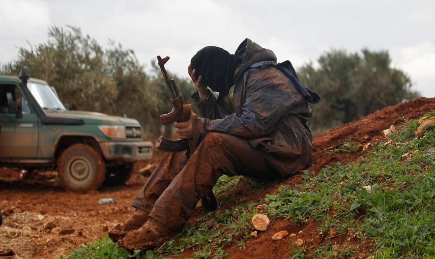 Un combatiente rebelde del frente Shamiya, cubierto de barro, sostiene su arma mientras se sienta, en el norte de Alepo. /RAMI ZAYAT (REUTERS)