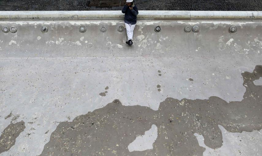 Un trabajador habla por su teléfono móvil mientras permanece sentado en el borde de la Fontana de Trevi, sin agua. REUTERS/Tony Gentile