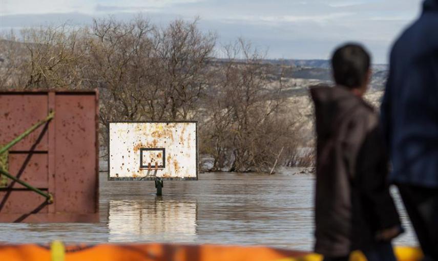 Varias personas observan un campo de baloncesto anegado por la crecida del río Ebro, hoy en la localidad de Cabañas de Ebro. Las motas de contención están aguantado el caudal del Ebro y la noche ha transcurrido en los pueblos de la ribera zaragozana "sin