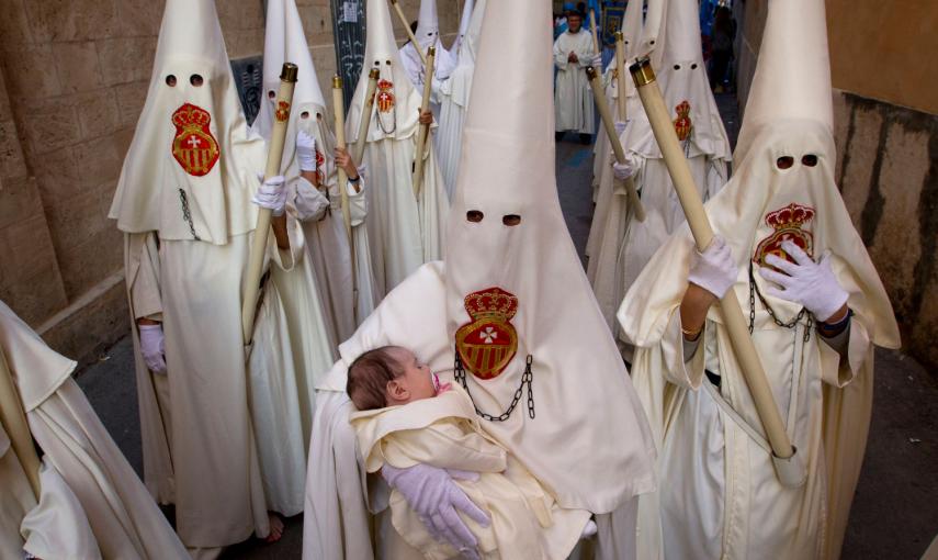 Un miembro de la hermandad del Cristo de la Sangre, lleva a un bebé durante una procesión de Pascua, en Palma de Mallorca. /JAIME REINA (AFP)