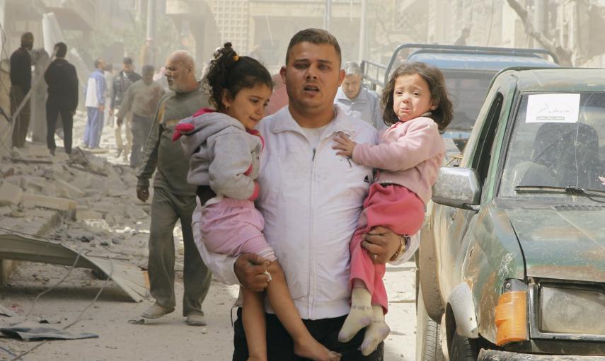 Un hombre coge a dos niñas mientras se apresura a buscar un refugio después de que el barrio de al-Thawra haya sido golpeado./ REUTERS / Ammar Abdullah
