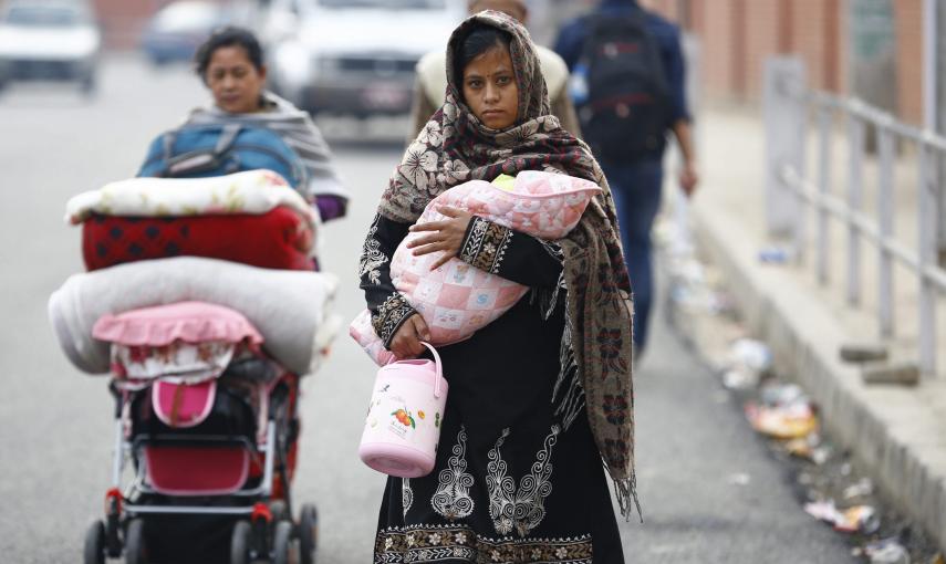 Una mujer lleva a su hijo en brazos mientras su madre carga con un carrito lleno de mantas al regresar a su casa en Katmandú./ EFE/Narendra Shrestha