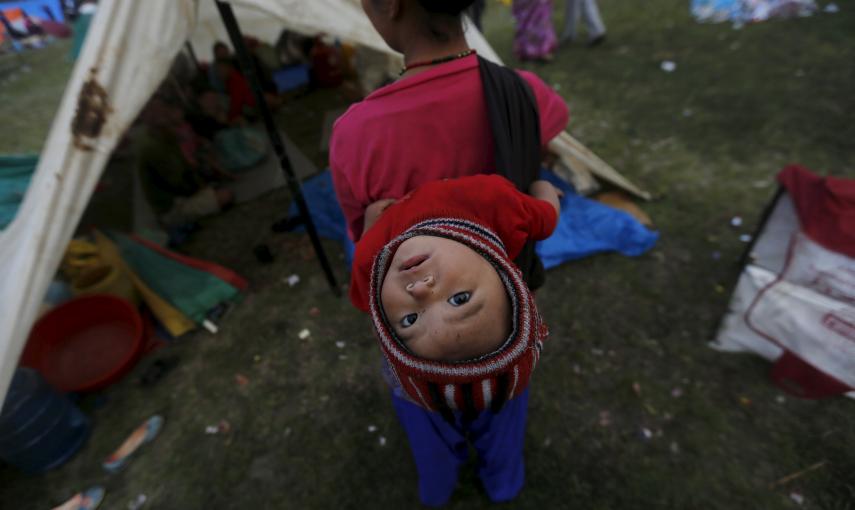 Una víctima del terremoto lleva a su bebe en la espalda mientras permanece fuera de su refugio improvisado en las afueras de Katmandú./  REUTERS/Adnan Abidi