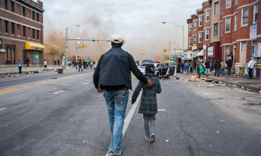 Un hombre camina con su hija en medio de las protestas por la muerte de Freddie Gray. EFE