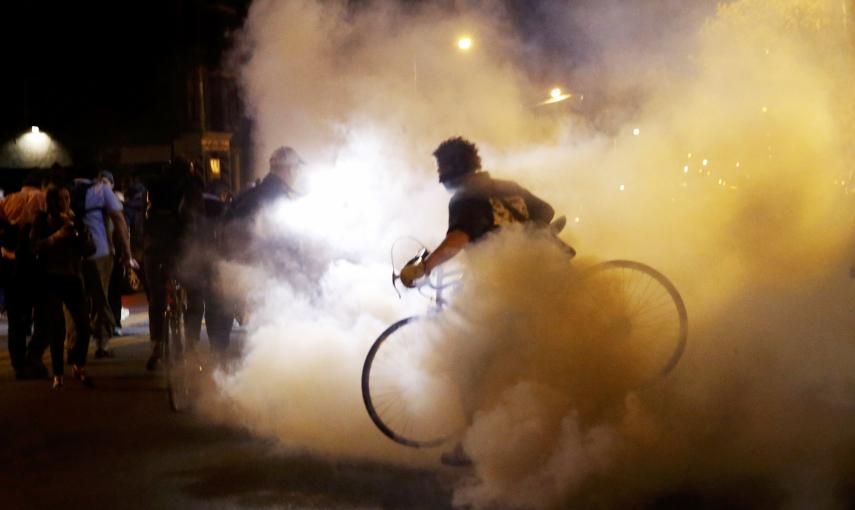 A protester moves his bicycle as clouds of smoke and crowd control agents rise shortly after the deadline for a city-wide curfew passed in Baltimore. REUTERS/Shannon Stapleton