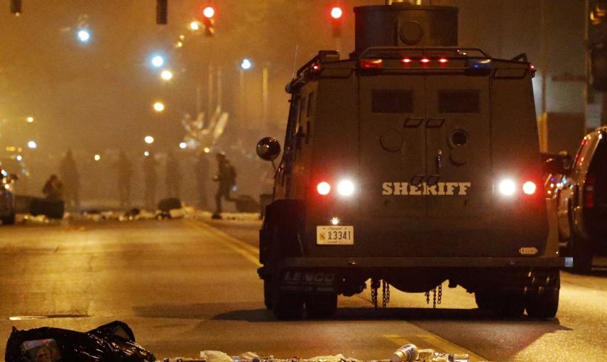 A police armoured car moves down a street as clouds of smoke and crowd control agents rise shortly after the deadline for a city-wide curfew passed in Baltimore. REUTERS/Jim Bourg