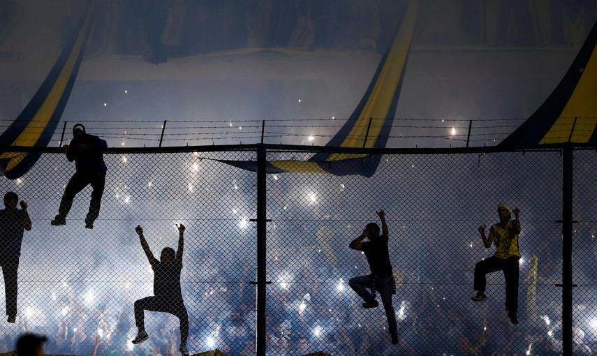 Hinchas del Boca Junios suben a la verja mientras animan a su equipo antes del partido de la Copa Libertadores frente al River Plate, en Buenos Aires.- MARCOS BRINDICCI (REUTERS)