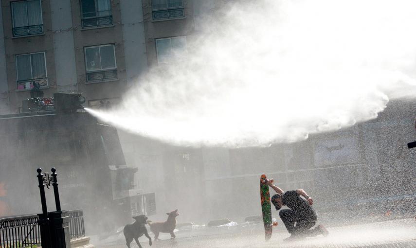 Un manifestante se protege con su monopatín de un chorro de agua a presión lanzado por los antidisturbios durante una manifestación para exigir cambios en el sistema educativo de Santiago (Chile).- CATALINA ALLEN (REUTERS)