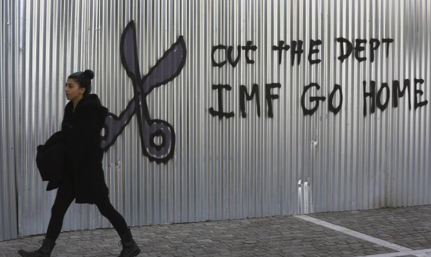 Una mujer pasea por el centro de Atenas junto a una pintura en contra del FMI.- REUTERS