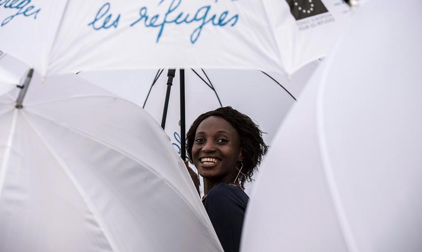 Una mujer sonríe mientras la gente se manifiesta sujetando paraguas blancos, con motivo del Día Mundial del Refugiado en Lyon- JEAN-PHILIPPE KSIAZEK (AFP)