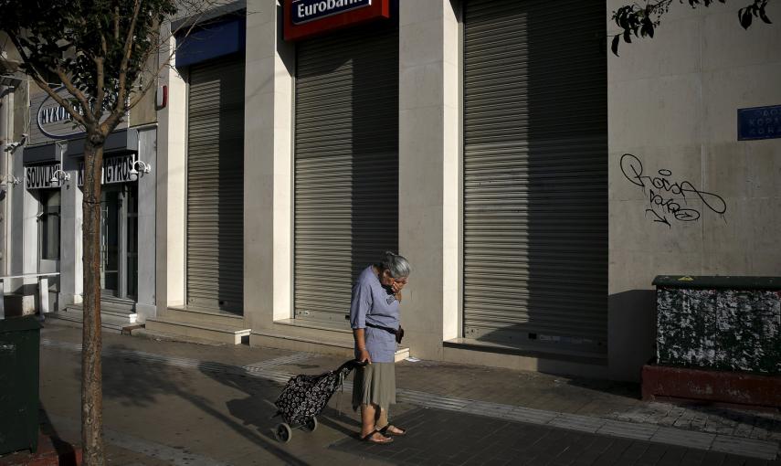 Una mujer que tira de un carrito de la compra se detiene frente a sucursal de Eurobank cerrada en Atenas, Grecia, tras declararse el control de capitales.  -REUTERS / Alkis Konstantinidis