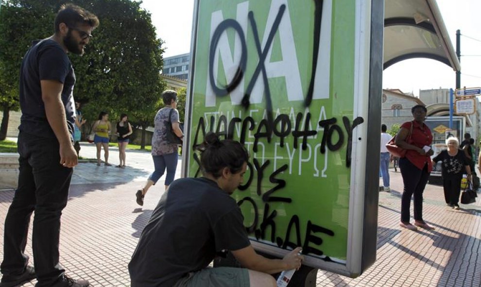 Un joven escribe con grafiti "No" sobre un cartel que pide el "Sí" en el referendum del domingo en una marquesina de autobús en Atenas. - EFE