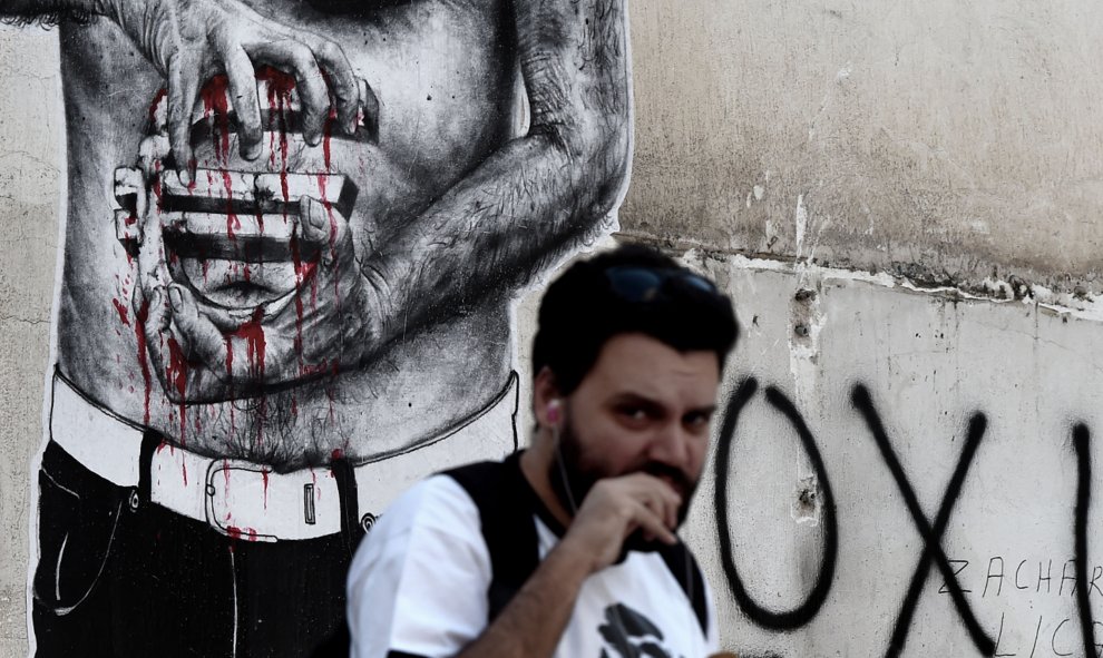 Un hombre pasa al lado de una pintada del símbolo del euro, en el centro de Atenas, hoy, el 14 de julio de 2015. AFP PHOTO / ARIS MESSINIS