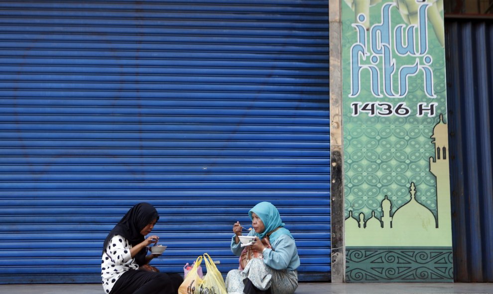 Dos mujeres almuerzan frente a un local que permanece cerrado con motivo de la festividad del Eid al-Fitr, en Yakarta (Indonesia) hoy, 21 de julio de 2015. El Banco Central Indonesio informó que la proyección de inflación en julio es de un 0,35% mensual y