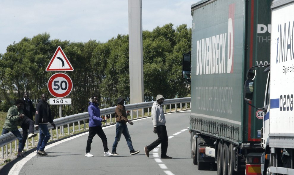 Varios inmigrantes cruzan una carretera cerca de la entrada del Eurotúnel, en Coquelles, cerca de Calais, Francia. EFE/YOAN VALAT