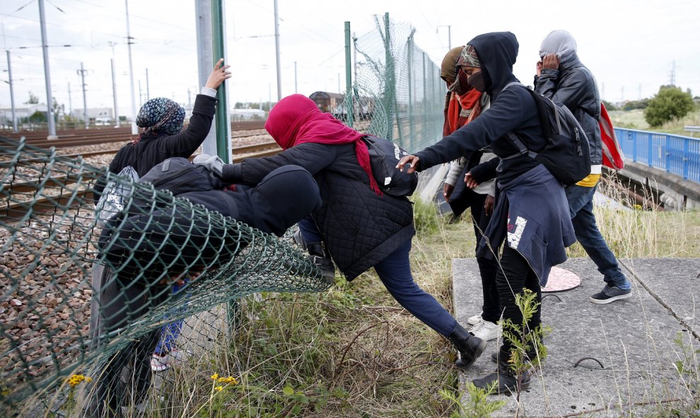 Inmigrantes cruzan una valla al tratar de llegar al tren que los conduciría a Inglaterra.  EFE/YOAN VALAT