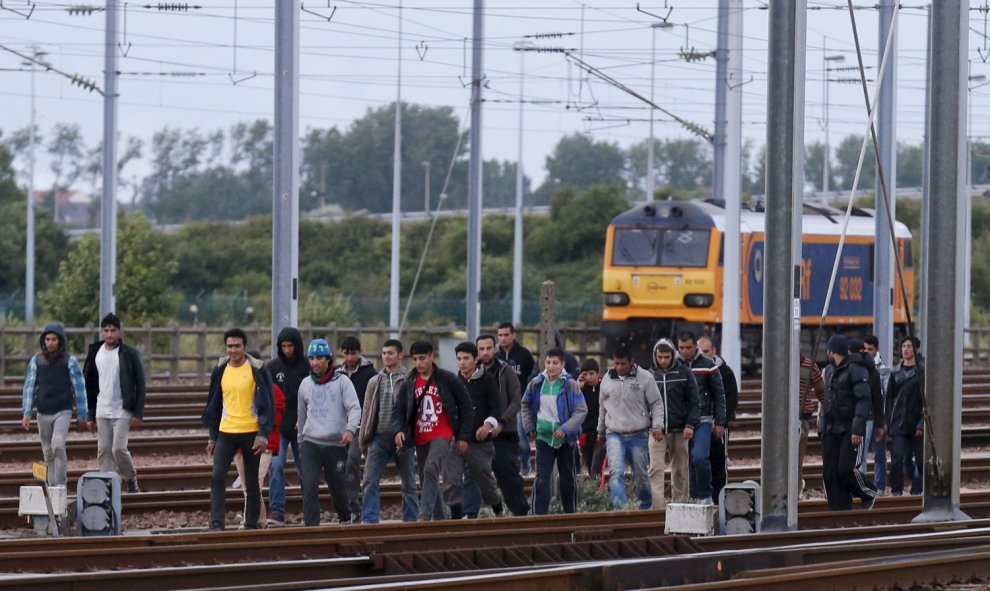 Inmigrantes caminan sobre una vía férrea para tratar de llegar al tren. REUTERS/Pascal Rossignol