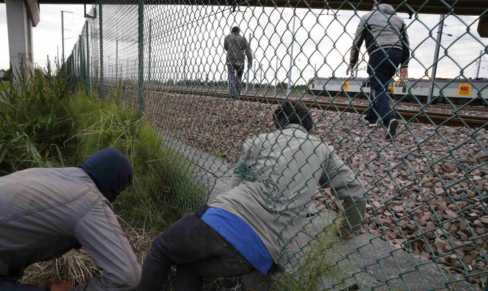 Inmigrantes cruzan una valla al tratar de llegar al tren que los conduce a Inglaterra . REUTERS/Pascal Rossignol