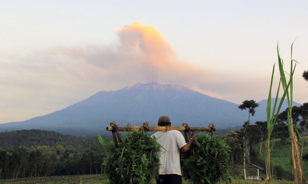 Un agricultor trabaja en el campo mientras que en el fondo de la imagen se ve cómo el volcán Monte Raung emite vapor y ceniza, en Banyuwangi, situada en el este de la isla de Java en Indonesia. AFP PHOTO