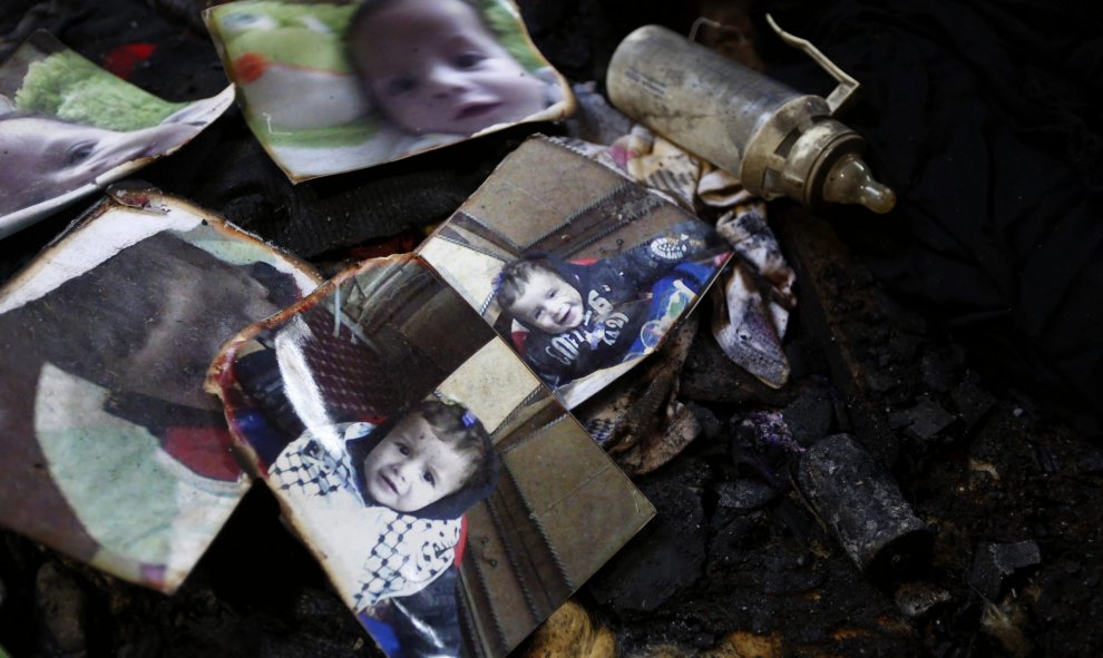 Un biberón descansa junto a las fotografías del bebé palestino de 18 meses Ali Dawabsha, que murió en un incendio provocado por colonos extremistas israelíes, entre los restos calcinados de su casa en la población palestina de Douma, junto a Nablus, 31 de