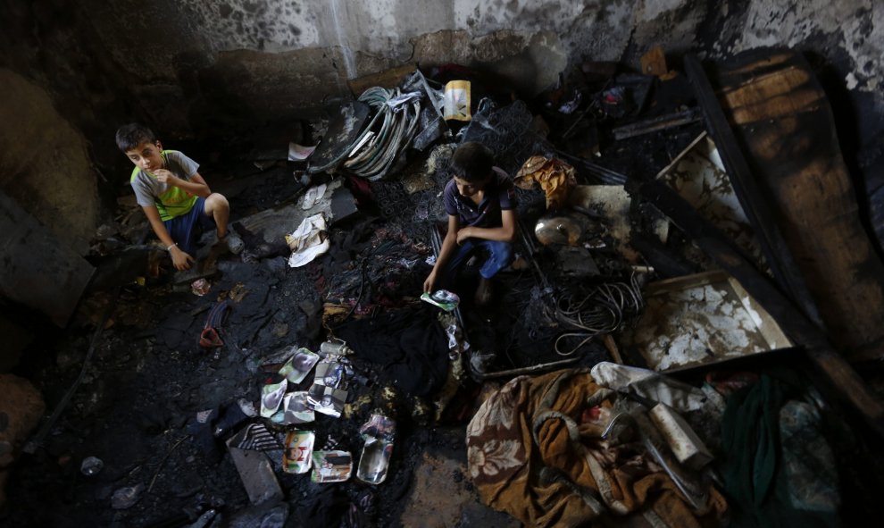 Un familiar observa una de las fotografías del bebé palestino de 18 meses Ali Dawabsha, que murió en un incendio provocado por colonos extremistas israelíes, entre los restos calcinados de su casa en la población palestina de Douma, junto a Nablus, hoy, 3