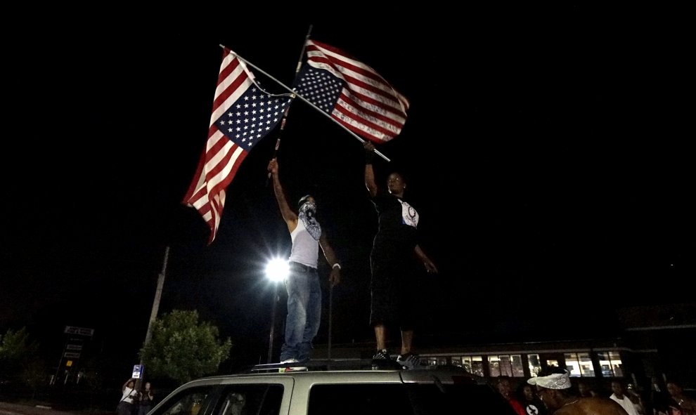 Un manifestante sostiene banderas de Estados Unidos al revés en la parte superior de un coche fuera del departamento de policía de Ferguson . REUTERS / Rick Wilking