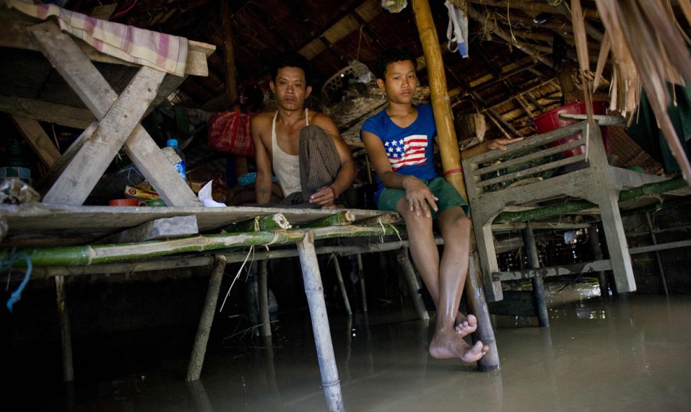 Unos habitantes se sientan dentro de su casa afectada por las inundaciones en el pueblo de Kyaut Ye cerca del pueblo de Hinthada en la región de Irrawaddy de Myanmar, el 10 de agosto de 2015. AFP PHOTO / Ye Aung