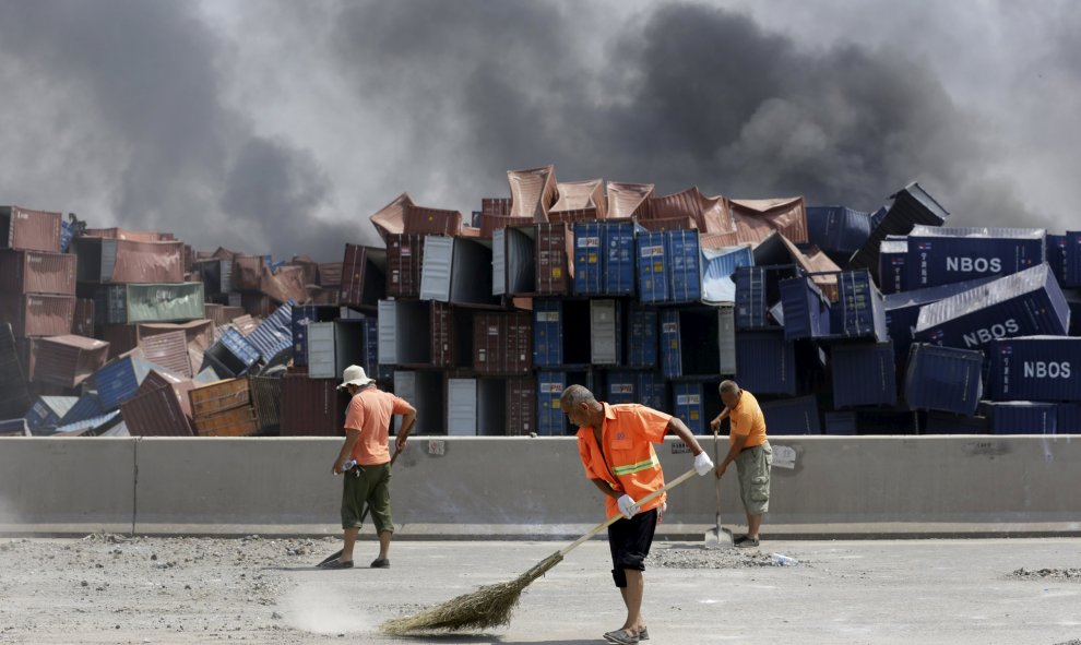 Varios empleados chinos trabajan para limpiar de piedras y polvo una carretera cerca del lugar de la explosión. REUTERS