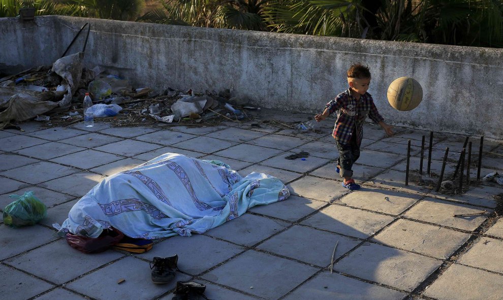 Un niño Pakistaní juega con una pelota mientras otro emigrante duerme en la terraza de un hotel abandonado en la isla griega de Cos, 13 de agosto de 2015. REUTERS / Alkis Konstantinidis