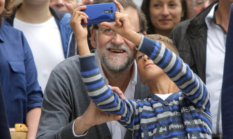 El presidente del Gobierno, Mariano Rajoy, que sigue de vacaciones en Galicia, posa para hacerse un "selfie" con un niño, durante la visita que realizó a la zona ganadera de Ódenes. EFE/Xoán Rey