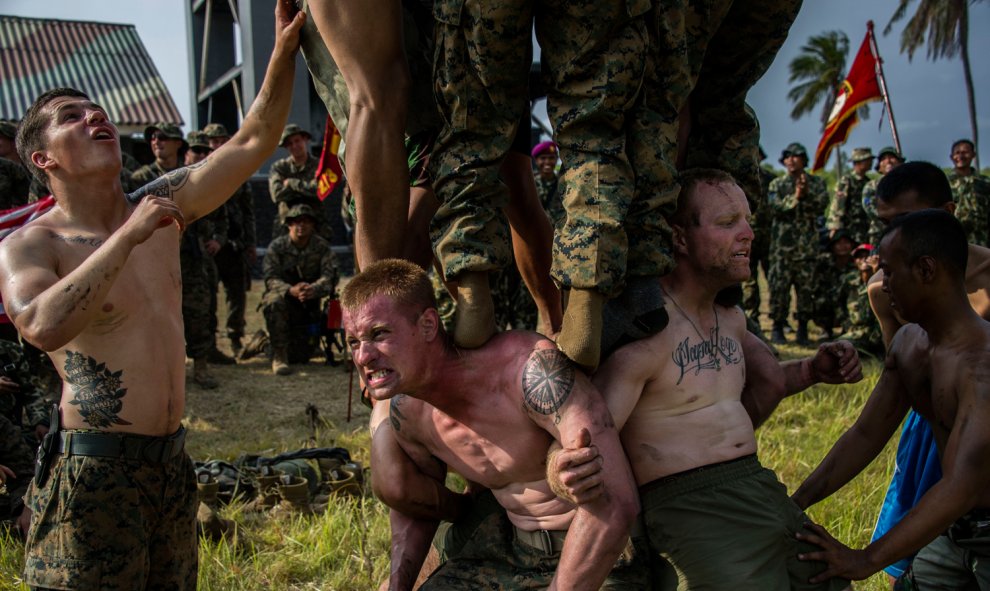 Marines estadounidenses juegan a un juego tradicional indonesio que consiste en escalar un poste resbaladizo para conseguir botellas de Coca-Cola, en la playa Banongan en Situbondo, en el este de la isla de Java.- AFP PHOTO / JUNI KRISWANTO