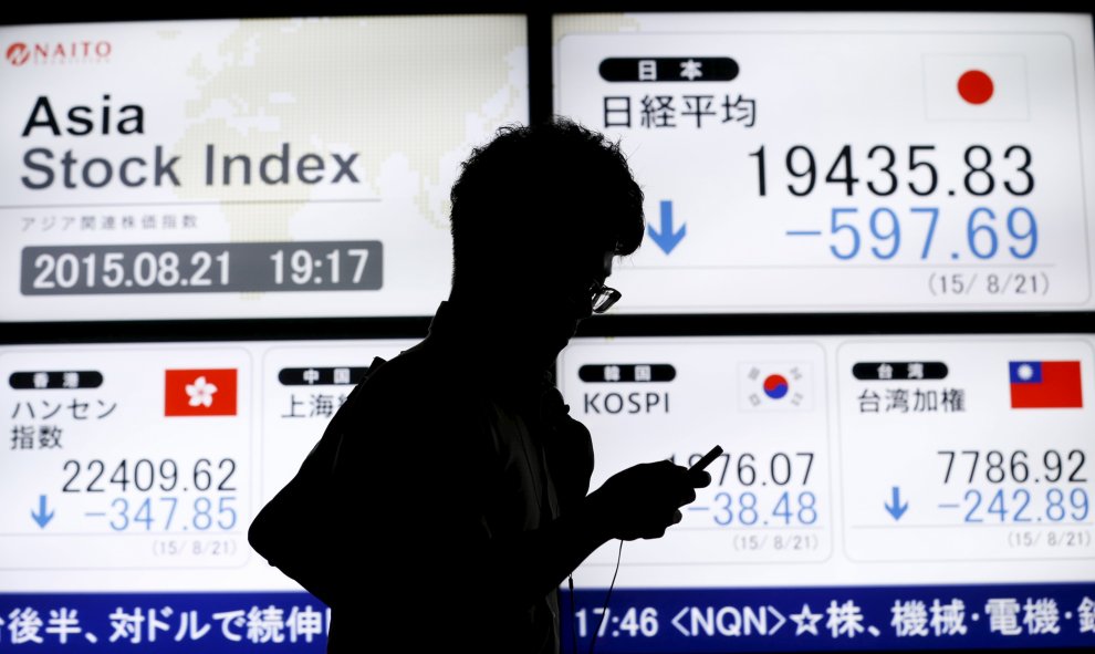 Un hombre pasa junto a un tablero electrónico que muestra el índice de precios de acciones de varios países asiáticos fuera de una casa de valores en Tokio. REUTERS