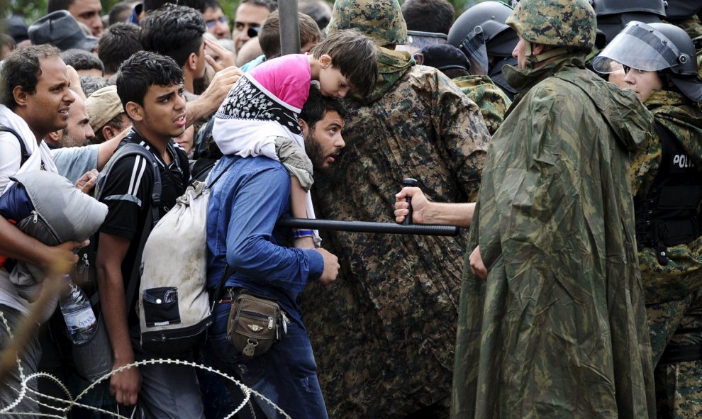 Un policía amenaza con la porra a una refugiado sirio que quiere cruzar la frontera de Grecia a Macedonia.- REUTERS/Ognen Teofilovski
