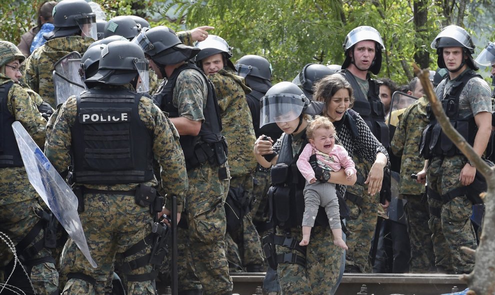 Una policía ayuda a cruzar el cordón a una refugiada y a su hija, en la frontera entre Grecia y Macedonia.-EPA/GEORGI LICOVSKI