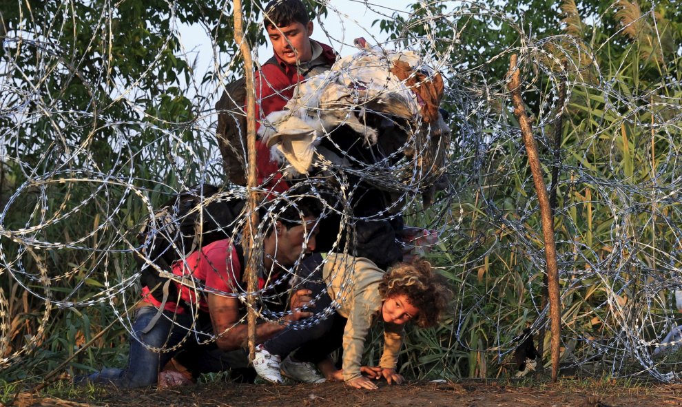 Una niña junto a su familia, refugiados sirios, trata de cruzar la valla de cuchillas instalada por Hungría en su frontera con Serbia, cerca Röszke.- REUTERS / Bernadett Szabo