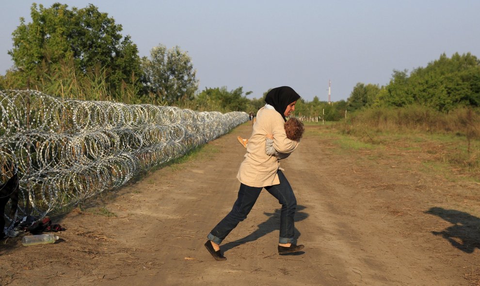 Una refugiada siria corre con su bebé en brazos después de atravesar la valla de cuchillas que ha levantado Hungría en su frontera con Serbia, cerca Röszke.- REUTERS / Bernadett Szabo