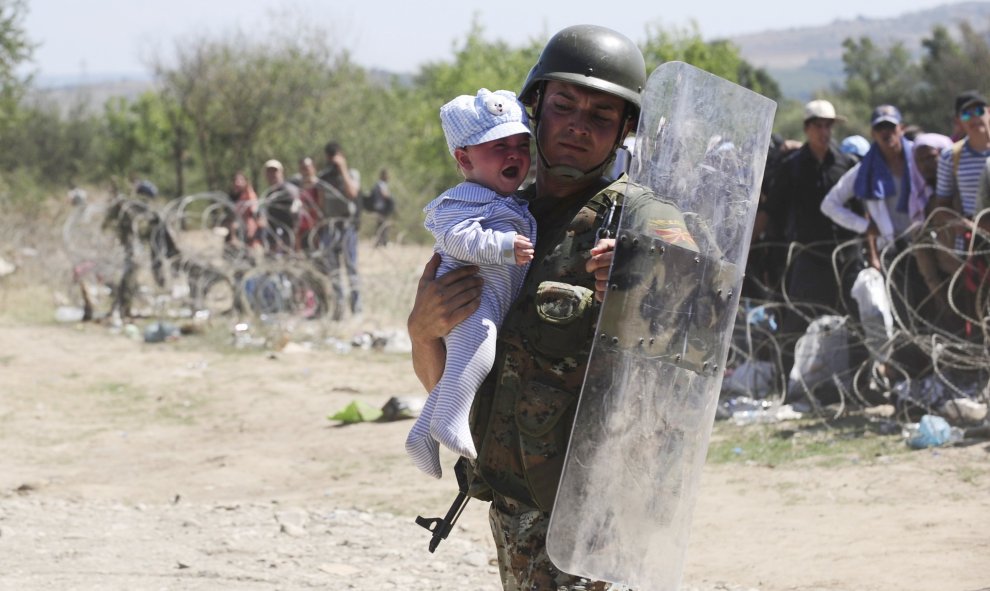 Un policía lleva un bebé a salvo mientras inmigrantes intentan cruzar la frontera de Macedonia y Grecia.  REUTERS/Ognen Teofilovski