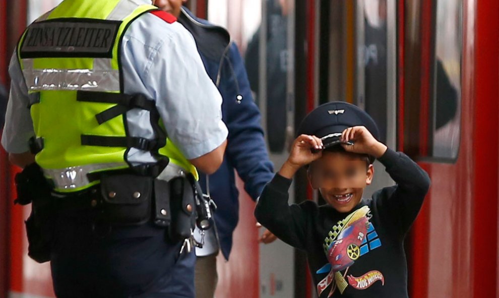 Un niño refugiado se pone la gorra de un agente de policía, a su llegada a la estación de tren de Múnich.- MICHAEL DALDER (REUTERS)