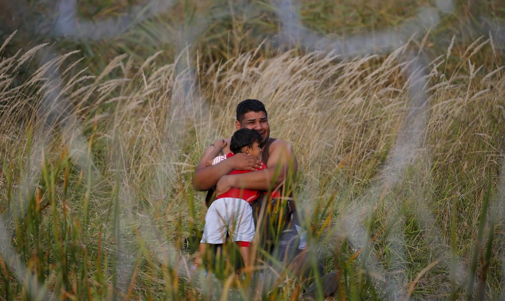 Un migrante que sostiene a su hijo en la parte serbia de la valla en Ásotthalom. REUTERS