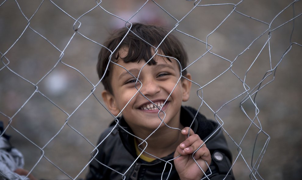 Un niño refugiado sonríe tras las verjas de un campamento mientras espera que otros inmigrantes y refugiados se registren después de cruzar la frontera entre Grecia y Macedonia cerca de Gevgelija el 22 de septiembre de 2015. AFP / NIKOLAY DOYCHINOV