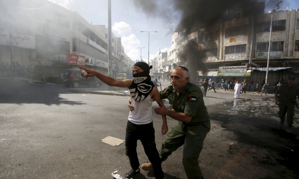 Un oficial de seguridad nacional palestino impide que un chico tire piedras a los soldados israelíes durante los enfrentamientos. Los policías y los palestinos israelíes se enfrentaron el domingo en Jerusalén, donde la violencia en las últimas semanas ha