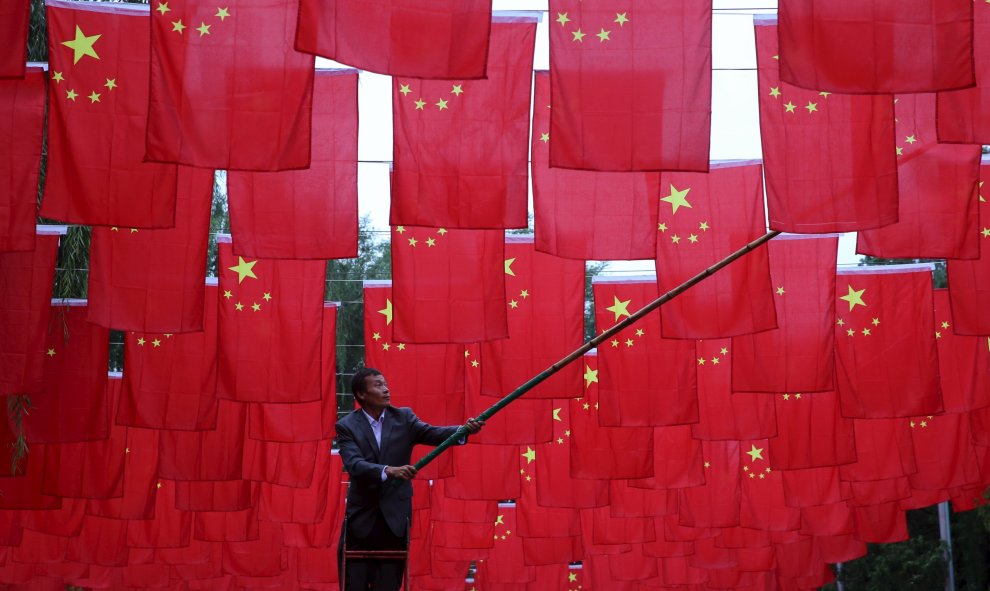 Un hombre cuelga banderas nacionales chinas para decorar un parque antes del Día Nacional de China que será el 1 de octubre, en Pekín.  REUTERS/China Daily